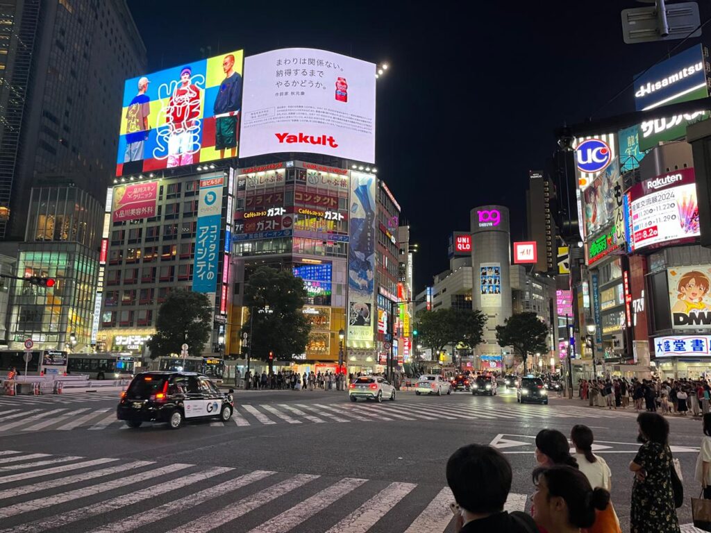 Multitud cruzando el famoso cruce de Shibuya bajo las luces de neón y pantallas gigantes.