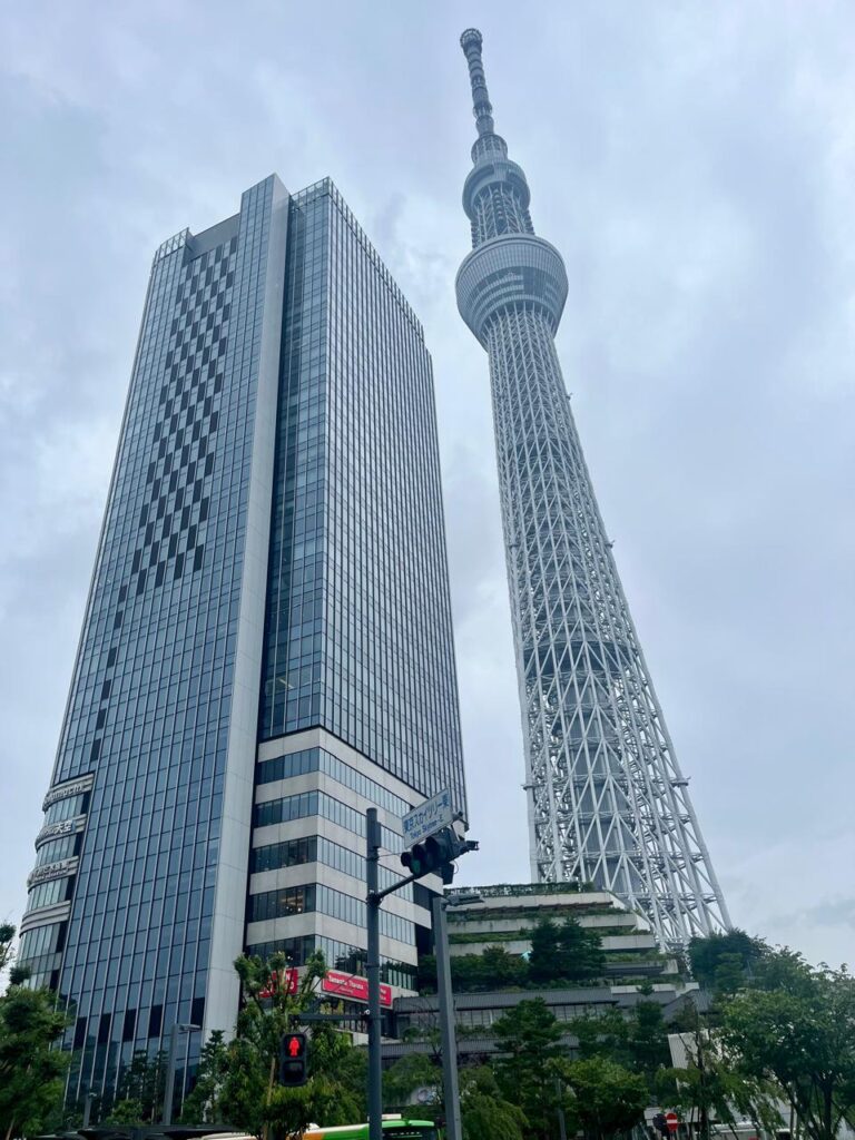 Tokio Skytree vista desde la calle, con edificios urbanos en primer plano y cielo despejado de fondo.